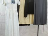 une robe blanche posée sur un portant, à côté d'un pantalon noir