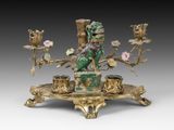 une image représentant une figurine dorée et verte ornée de fleurs, posée sur un socle