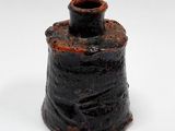 un petit vase noir au couvercle rouillé, posé sur une surface blanche