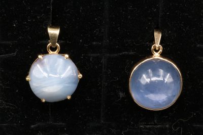 two gold pendants with blue and white stones on a black velvet surface