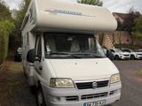 un camping-car blanc garé sur un parking à côté d'une haie