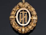 an image of a gold broochle with the letter t on it