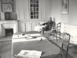 black and white photograph of a man sitting in a chair in a bedroom