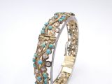 a close up of a gold and turquoise bracelet on a white background