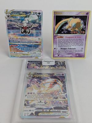 trois cartes Pokémon dans des pochettes en plastique posées sur une surface blanche