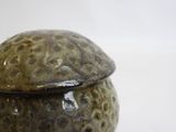 a brown and black vase with a lid on a white surface