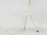 une photo d'une chaise en métal blanc devant un mur blanc