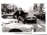 black and white photograph of a man sitting on a motorcycle in the middle of a busy city street