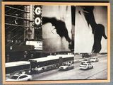 black and white photograph of a city street with cars, buses, and a giant billboard
