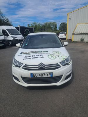 La voiture est garée sur le parking, avec d'autres véhicules en arrière-plan.