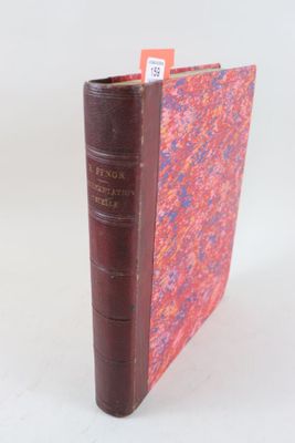 un vieux livre posé sur une table blanche à côté d'un livre rouge