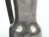 a silver pitcher sitting on a table next to a vase