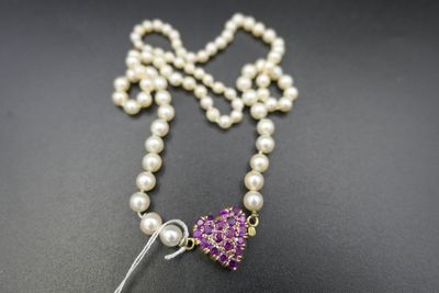 a close up of a necklace with pearls and a purple flower