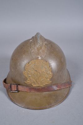un vieux casque orné d'un emblème doré, posé sur une surface blanche