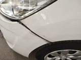 the front end of a white car with a dent in it ' s bumper