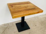 La table est en bois et possède un piètement en métal noir.
