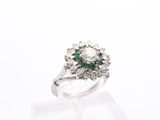 a close up of a diamond and emerald ring on a clear surface