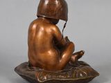 bronze figurine of a boy sitting on a pillow with a helmet on his head