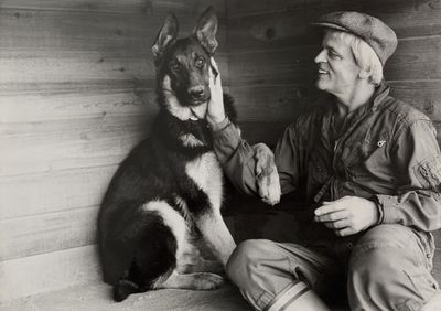 photo en noir et blanc d'un homme assis à côté d'un chien
