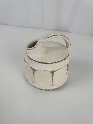 a white ceramic container with a handle on a white surface