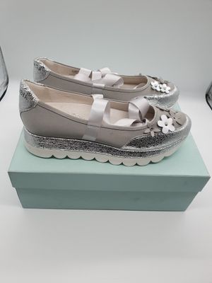 Des chaussures ornées de nœuds sont posées sur une boîte, à côté d'un verre de vin
