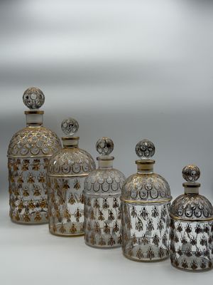 five glass jars with gold designs are lined up on a white surface