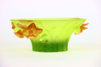 un vase vert contenant des fleurs orange, posé sur une surface blanche