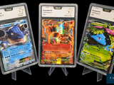 Trois cartes Pokémon sont exposées dans des pochettes en plastique sur un fond noir.