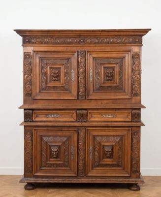 une vieille armoire en bois ornée de sculptures sur le dessus, posée sur un parquet en bois massif