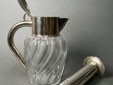 a silver and glass pitcher with a spoon next to it
