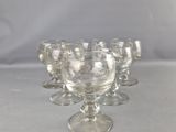 six verres à pied en verre transparent sont alignés sur une surface blanche