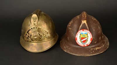 une paire de casques de pompier anciens sur fond noir, avec un blason au centre