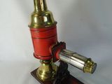 un microscope ancien en laiton et rouge, posé sur un socle en bois