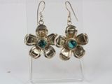 silver flower earrings with green stones on a clear acrylic stand