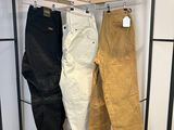 trois paires de pantalons suspendues à un portant dans un magasin de vêtements
