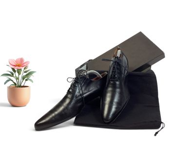 chaussures en cuir noires pour homme, accompagnées d'un sac noir et d'une fleur rose