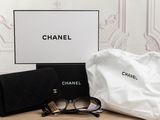 chanel eyeglasses and a bag on a table in front of a wallpapered wall