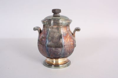 a silver and brown vase with a lid on a table