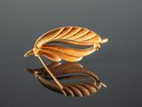 a close up of a gold leaf broochle on a reflective surface