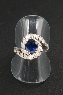 une photo d'une bague sertie d'un saphir bleu et de diamants, posée sur un présentoir transparent