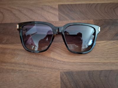 des lunettes de soleil posées sur une table en bois, avec une personne en train de prendre une photo