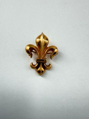 un gros plan d'une broche en forme de fleur de lys dorée posée sur une surface blanche