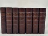 six old books lined up in a row on a white surface
