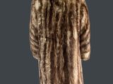 une femme vêtue d'un manteau de fourrure marron, debout sur un fond gris