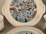 a plate with a picture of a village on it next to a bowl and a plate with a cup