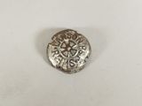 une pièce d'argent ornée d'une croix, posée sur une surface blanche
