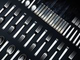 de nombreuses fourchettes et cuillères disposées sur une surface noire