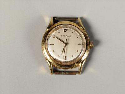 une montre-bracelet en or avec un cadran blanc sur une surface blanche