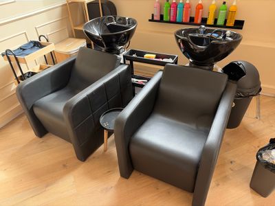 deux chaises noires dans un salon de coiffure, avec des sèche-cheveux accrochés au mur