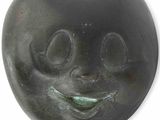 une sculpture noire représentant un visage souriant sur fond blanc